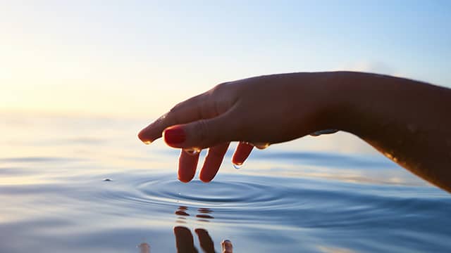 A woman's hand making ripples on the surface of the water.