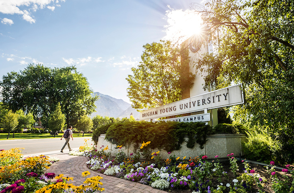 A sunlit, flower-filled photo of the Brigham Young University entrance sign.