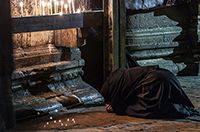 A nun bows in worship on holy ground near a row of candles in the Church of the Holy Sepulcher in Jerusalem.