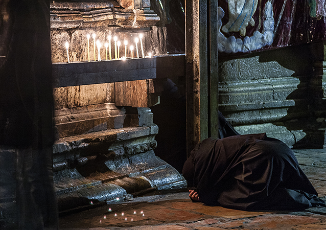 A nun bows in worship near a row of candles in the Church of the Holy Sepulcher in Jerusalem. 