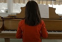 Young girl playing the piano, signifying the relationship between God's grace and a parent providing music lessons for their child.