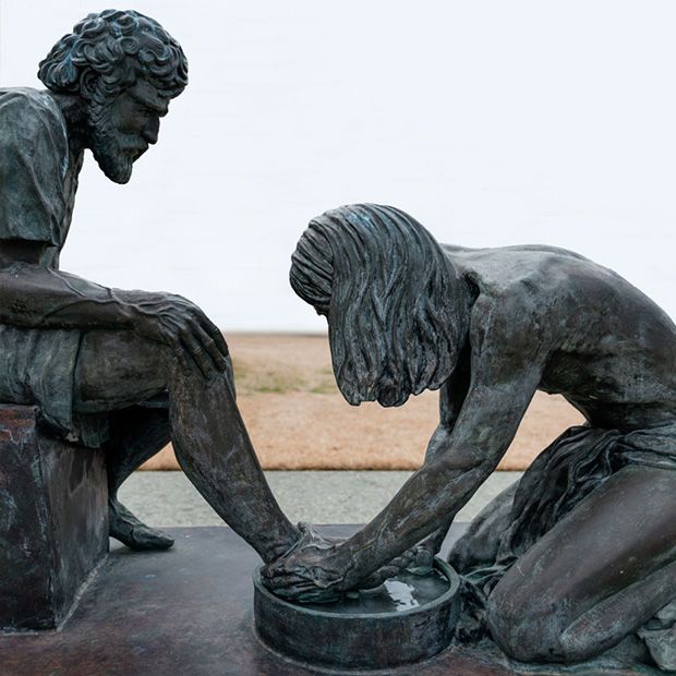 Bronze statue of Jesus Christ washing the feet of one of his apostles, an example of the charity.