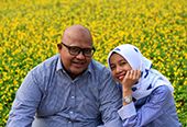 A husband and wife smiling together in a field of flowers.
