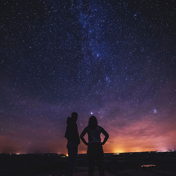 Silhouette of a man and woman under a starry sky, standing apart from each other.