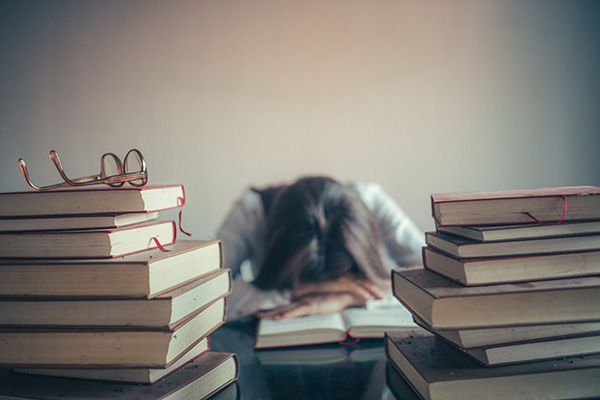 Female student laying her head on her desk, surrounded by books.
