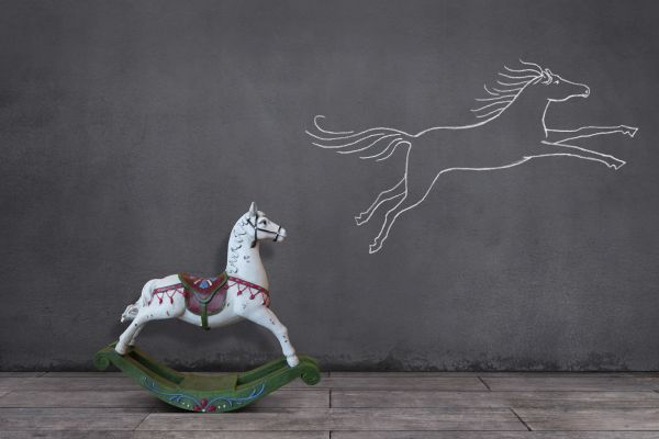 Side view of wooden rocking horse on wooden floor with running horse sketched on the wall.