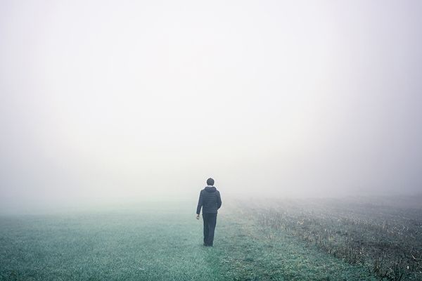 A solitary man walks on a green pasture into fog